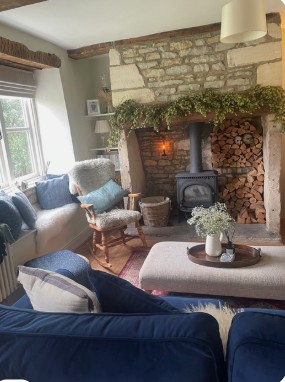 Cozy living room with stone fireplace, wood stove, blue upholstered furniture, hop garland decorations, and large window