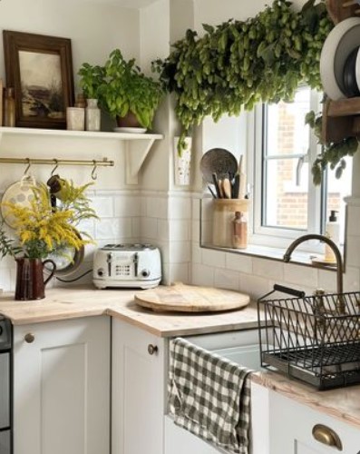 Farmhouse kitchen with white cabinets, wooden countertops, hop garland above window, yellow flowers, black dish rack, and gingham towel